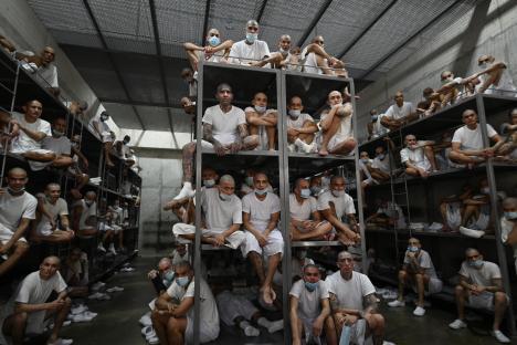Inmates wearing masks in a crowded prison cell block.