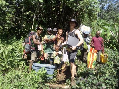 A researcher and local people carrying supplies through a tropical forest.