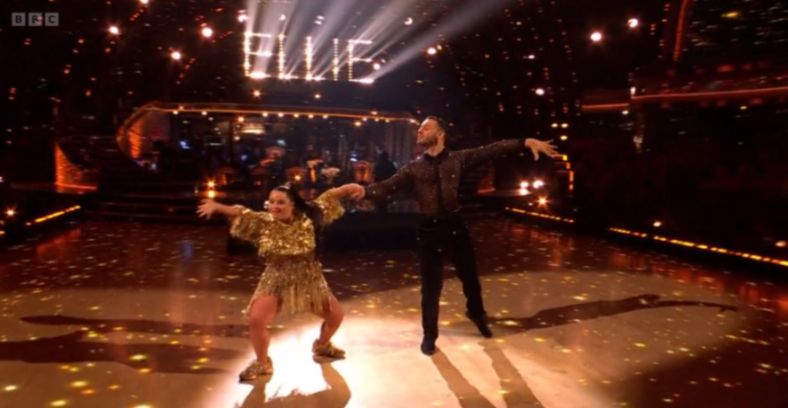 Ellie Simmonds and her dance partner performing on stage under bright lights, with the name "ELLIE" illuminated in the background.