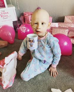 Young girl with a shaved head and nasal cannula holding a personalized mug.