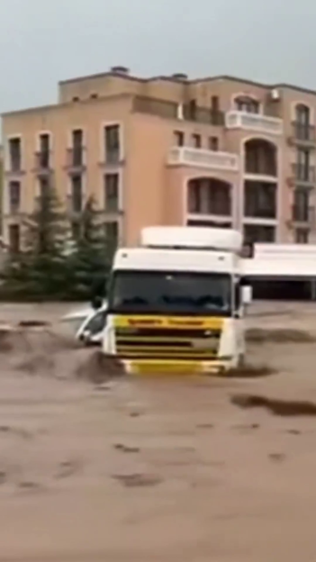 A semi-truck partially submerged in muddy floodwaters in front of a hotel.