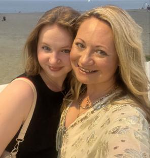 A mother and daughter pose for a photo on a beach.
