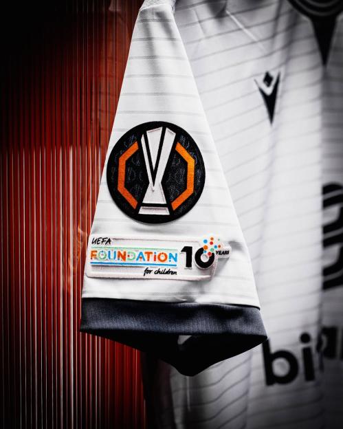 Close-up of a white soccer jersey sleeve with UEFA Europa League and UEFA Foundation for Children 10 Years patches.