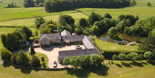 Aerial view of a large country house with surrounding gardens and pond.