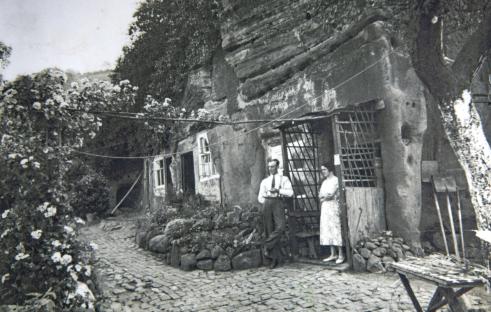 Black and white photo of a man and woman standing outside a rock house.