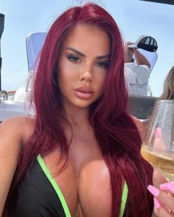 Woman with long red hair on a boat, holding a glass of wine.