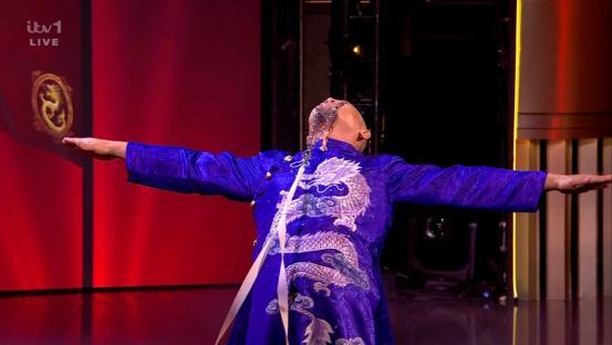 Person in a blue dragon-embroidered robe performing on a stage.