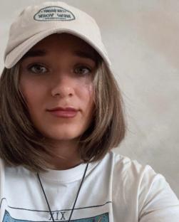Woman wearing a beige baseball cap and white t-shirt.