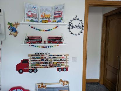 Child's room wall with toy cars, buses, and framed prints.