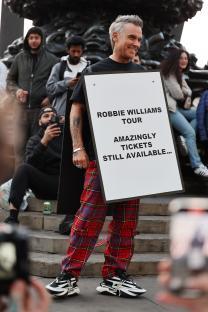 Robbie Williams holding a sign advertising his tour.