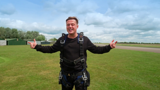 Man in skydiving gear gesturing at airfield.