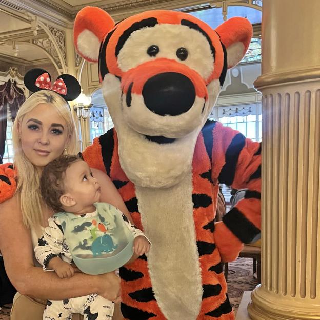 Jodie Weston with her son Koa-Zayde, wearing Minnie Mouse ears, posing next to a person in a Tigger costume.