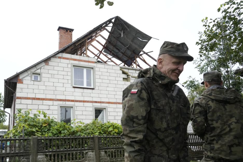 Polish territorial defense officers near a damaged house.