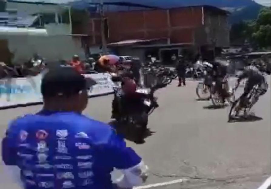 Cyclists crashing after a police officer on a motorcycle cuts them off during a race.