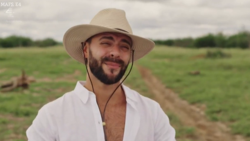 A smiling man in a straw hat and white shirt in a field.