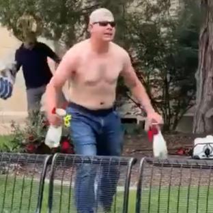 Shirtless man carrying bottles runs past a park bench.