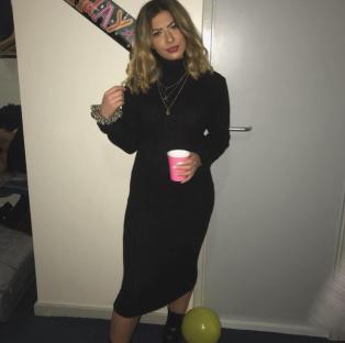 Woman in black sweater dress holding a pink cup.