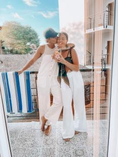 Two women kissing on a balcony, reflected in a glass door.