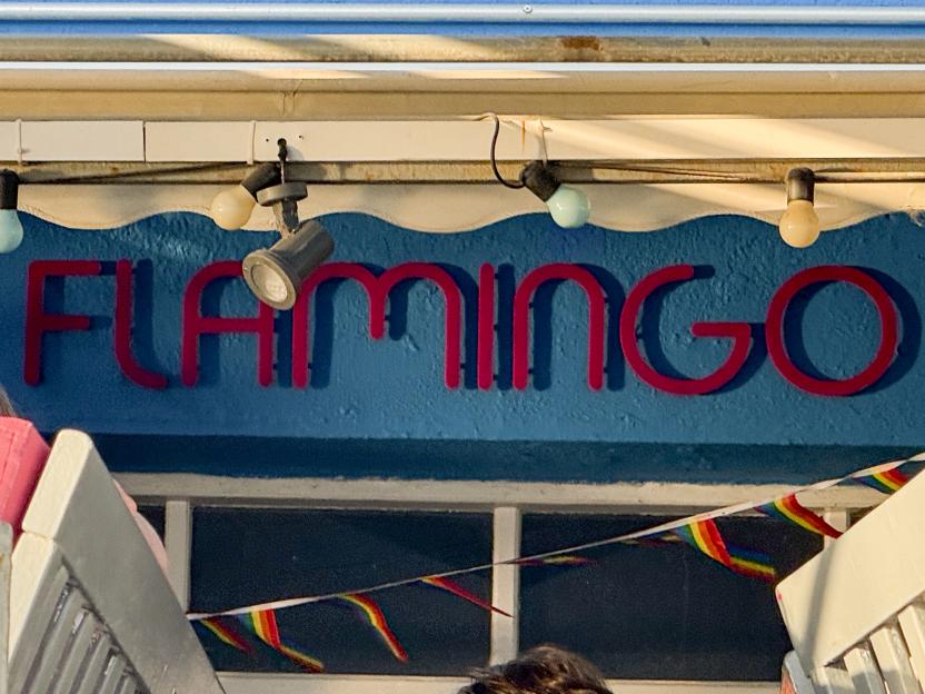 "FLAMINGO" bar sign with a rainbow flag banner in the foreground.