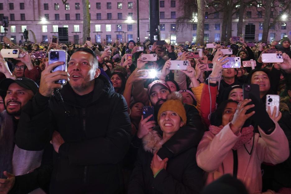 People looking up, watching, and taking photos as fireworks light up the sky around the London Eye to celebrate the New Year.