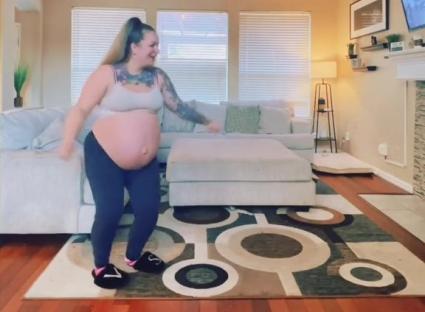 A heavily pregnant woman dances in her living room.