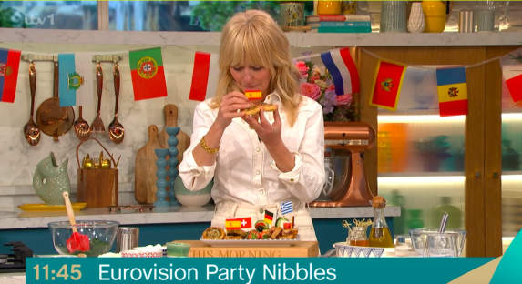 A woman on a cooking show holds up Eurovision-themed party nibbles.