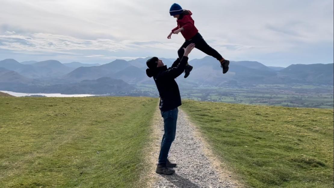 Andy Smith holding his daughter Emily in the air in a scenic mountain landscape.