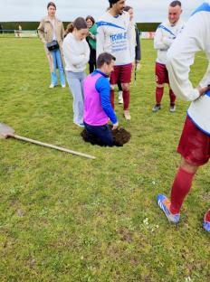 Soccer players gathered around a player filling a sinkhole on the field with a shovel.