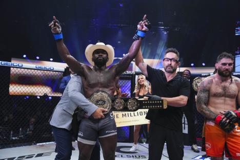 A victorious mixed martial arts fighter raises his arms in celebration, holding a championship belt.