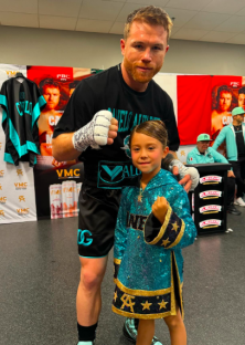 A boxer poses with a young girl wearing a boxing robe.