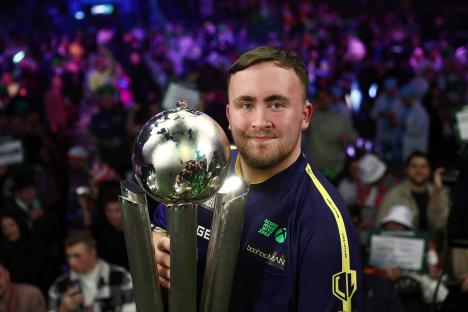Luke Littler holding the Sid Waddell Trophy after winning a darts championship.