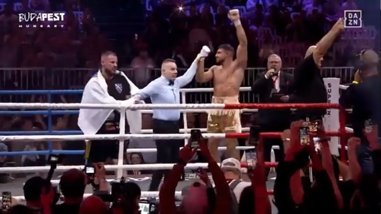 A boxer raises his arm in victory in a boxing ring.