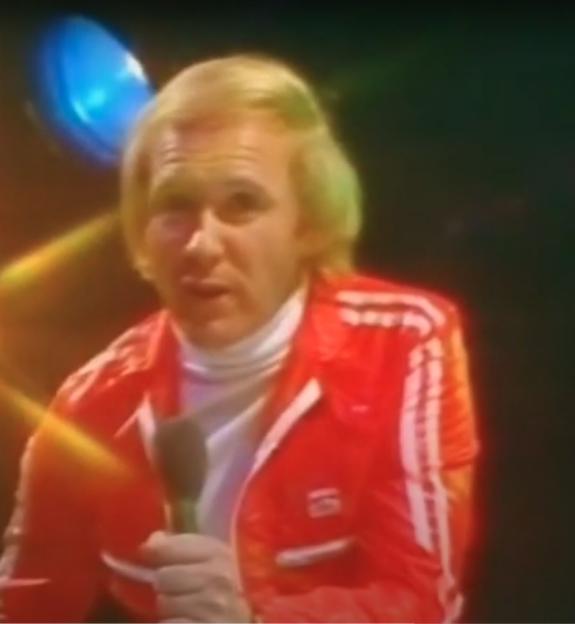 A man in a red adidas jacket holding a microphone