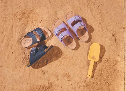 Children's sandals in sand with a small shovel.
