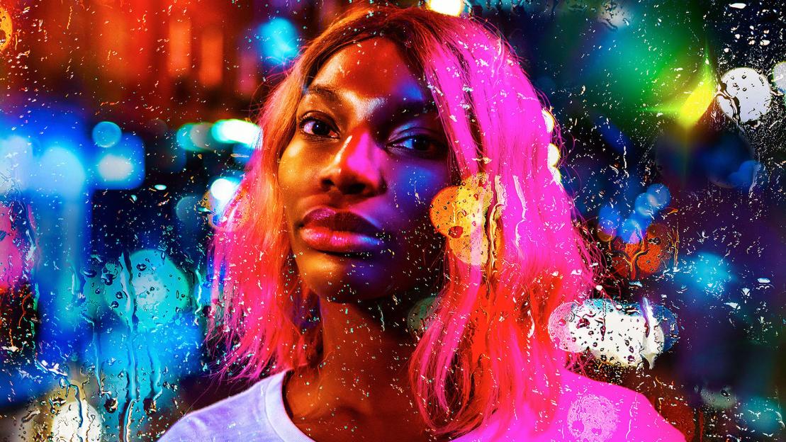 Michaela Coel in "I May Destroy You" with pink hair, looking through a rainy window at city lights.