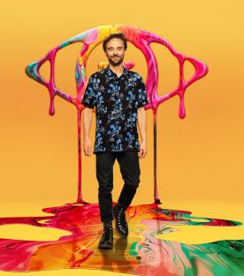Jack P. Shepherd walking in front of a large, colorful, paint-like eye.