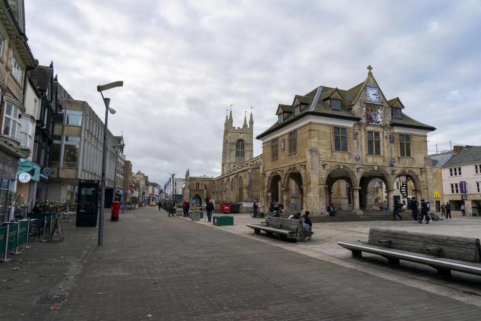 View of Peterborough city centre, with a large, old stone building with arches on the right, and a tall church tower in the background.