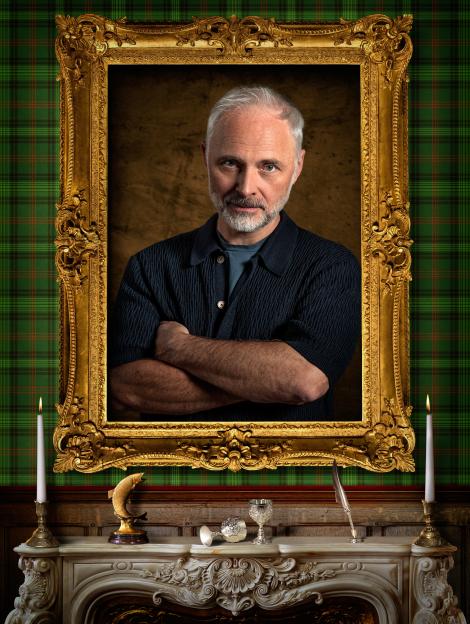Mark Bonnar in a gilded frame above a fireplace, flanked by candles, with green plaid wallpaper in the background.