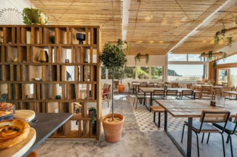 Interior view of a restaurant with wooden tables and chairs, a wooden room divider, and a view of the ocean.