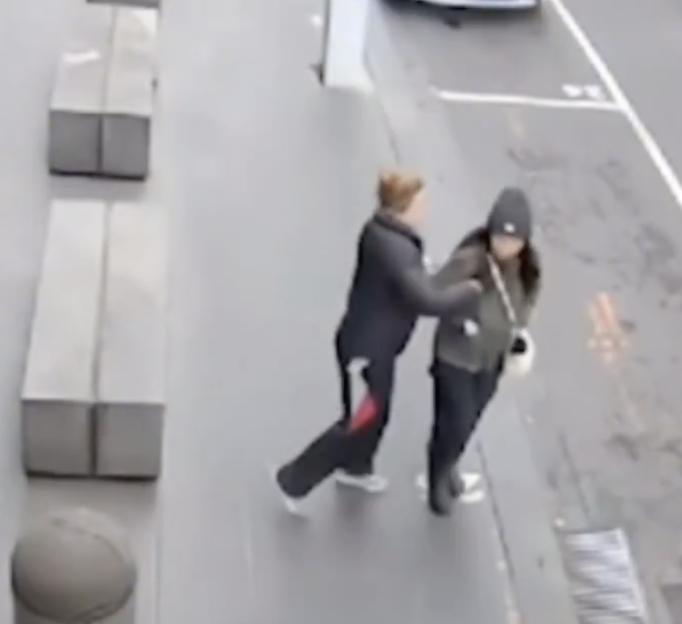 Two people engaged in a physical altercation on a sidewalk.