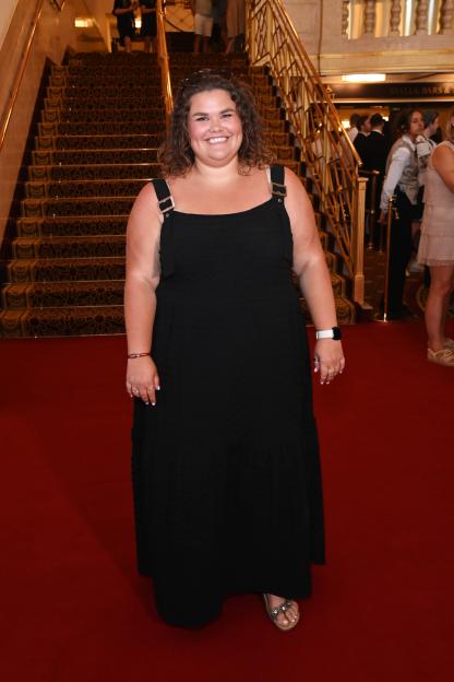 Amy Tapper smiles while posing on a red carpet at the Gala Night performance of "Grease The Musical".