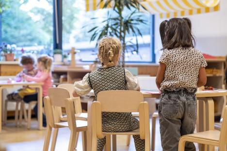 Rear view of preschool children sitting at a table in a classroom.