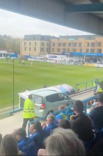 Soccer game viewed from the stands; a light green car is parked near the sidelines.