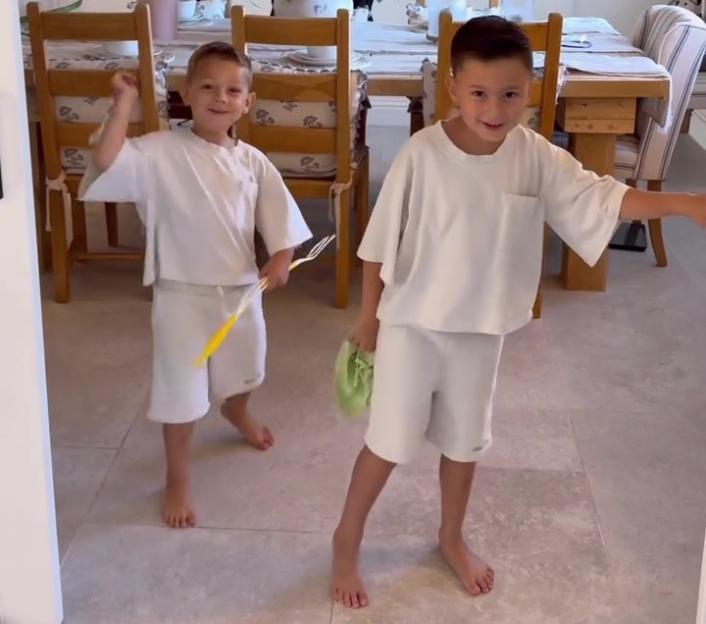 Two young boys in white outfits playing in a dining room.