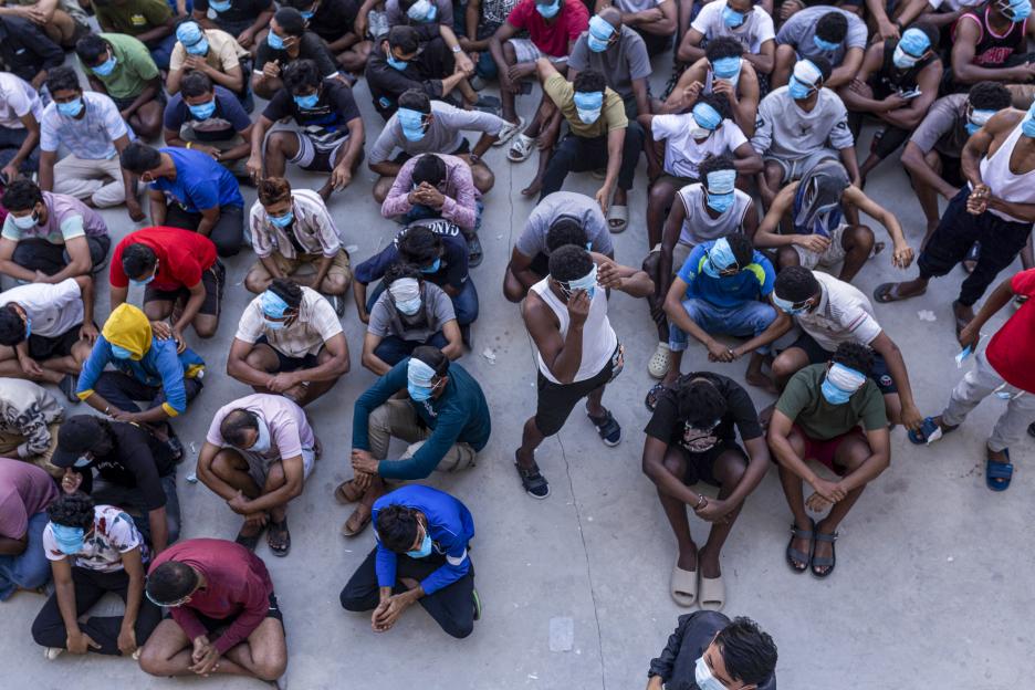 Alleged scam center workers and victims sit on the ground, some with masks over their eyes, during a crackdown operation.