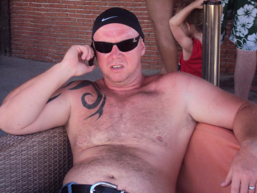 Man with tattoos on his shoulder and chest talking on a cell phone.