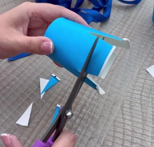 Hands using scissors to cut a blue paper tube for a birthday party favor.