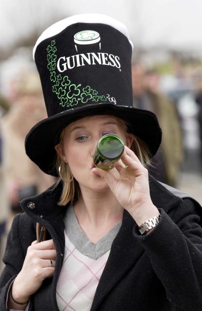 Racegoer wearing a Guinness hat and drinking Guinness on St. Patrick's Day at Cheltenham Races.