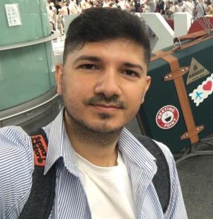 Man in striped shirt with a large suitcase in the background.