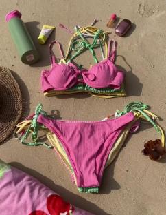 Pink bikini and beach towel on sand.
